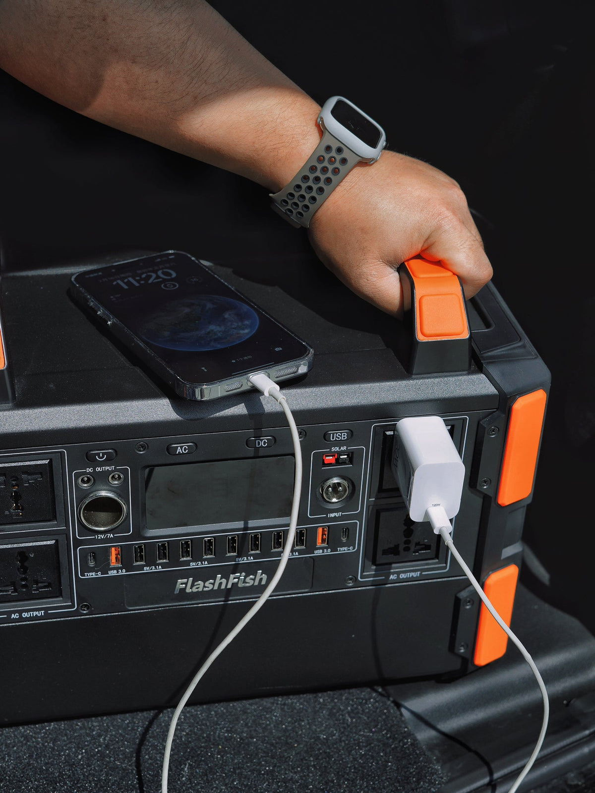 Hand gripping the orange handle of a FlashFish station with a phone resting on top