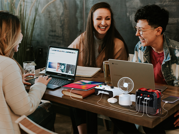 Three people sit around a table with a laptop, phone, small fan and portable power station.