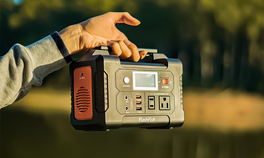 A hand carrying a FlashFish E200 portable power station against a blurred outdoor background.