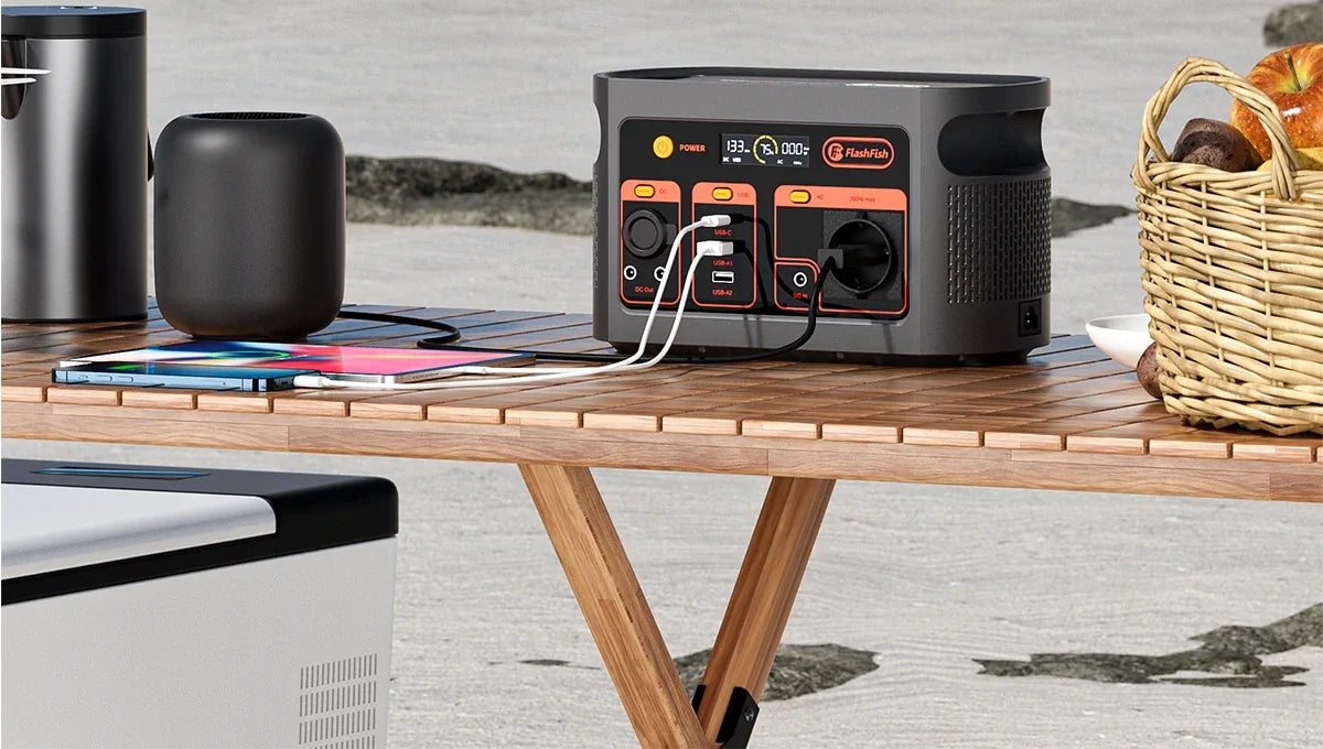 A portable power station, tablet, speaker and picnic basket on an outdoor table.