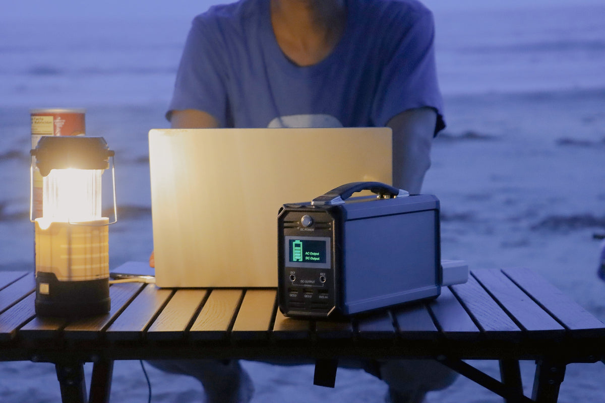 Person using a laptop beside a portable power station and table light outdoors