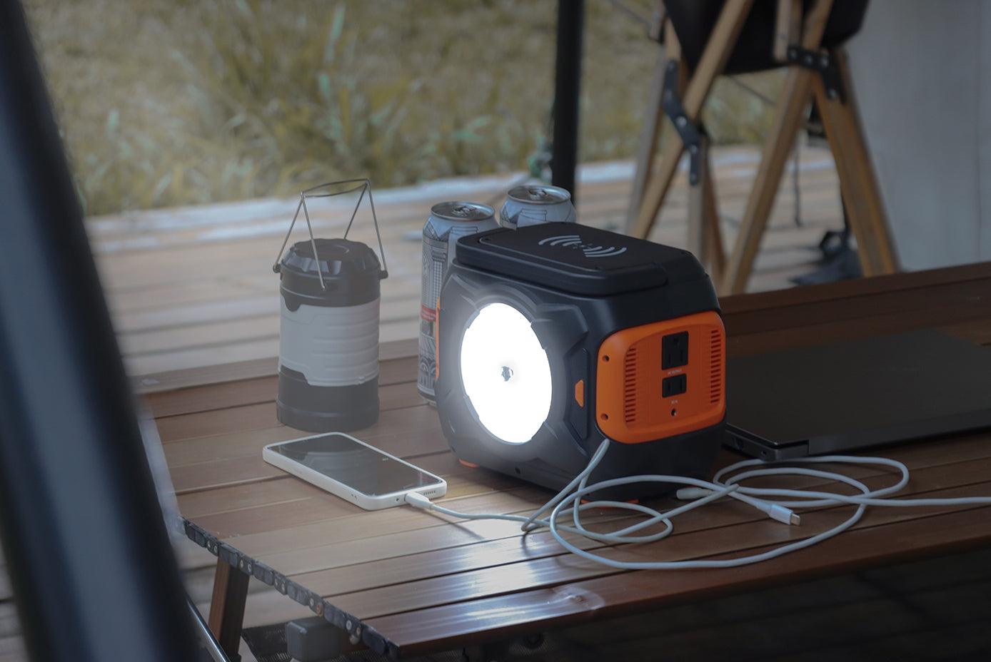 Portable power station charging a phone beside a lamp and laptop