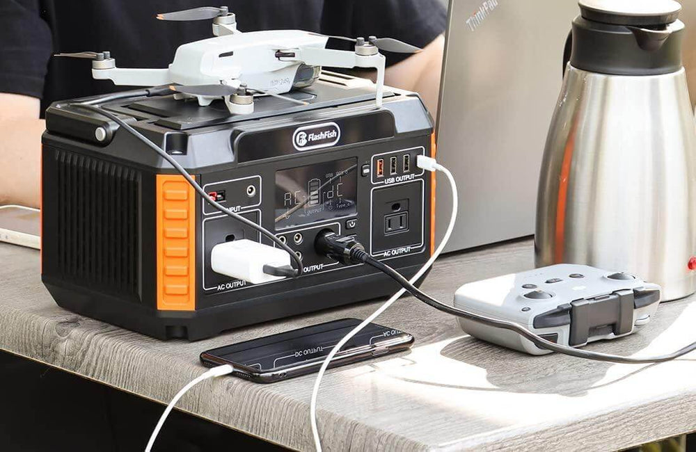 FlashFish portable power station beside a laptop, phone, controller, and camera drone on a table