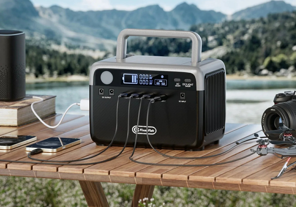 FlashFish portable power station on an outdoor wooden table with phones and a camera