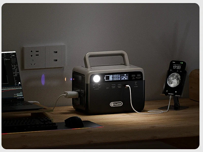 Portable power station with an illuminated display on a desk beside a laptop and phone.