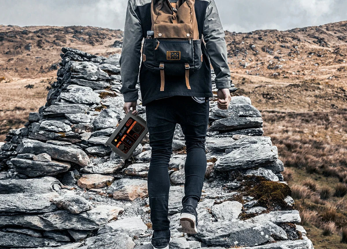 A backpacker carries a portable power station along a rocky path.