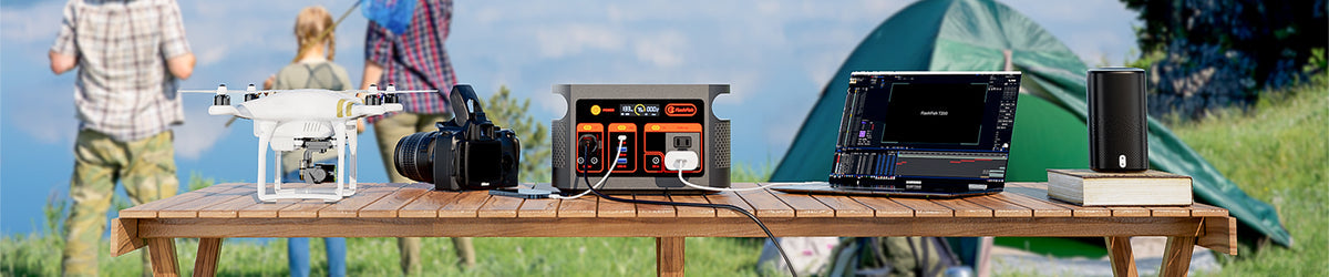 FlashFish portable power station with a laptop, camera, and small electronics on an outdoor table