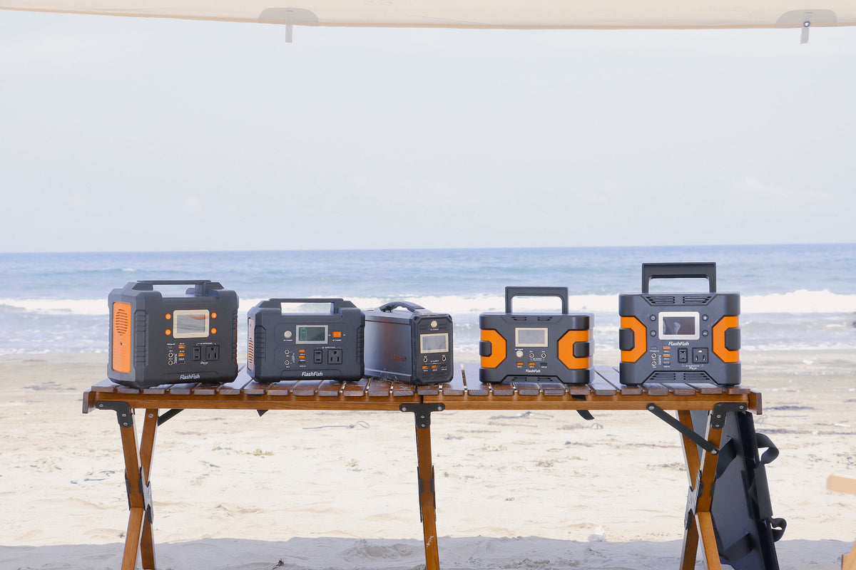 Five FlashFish portable power stations arranged on a wooden table beside the beach