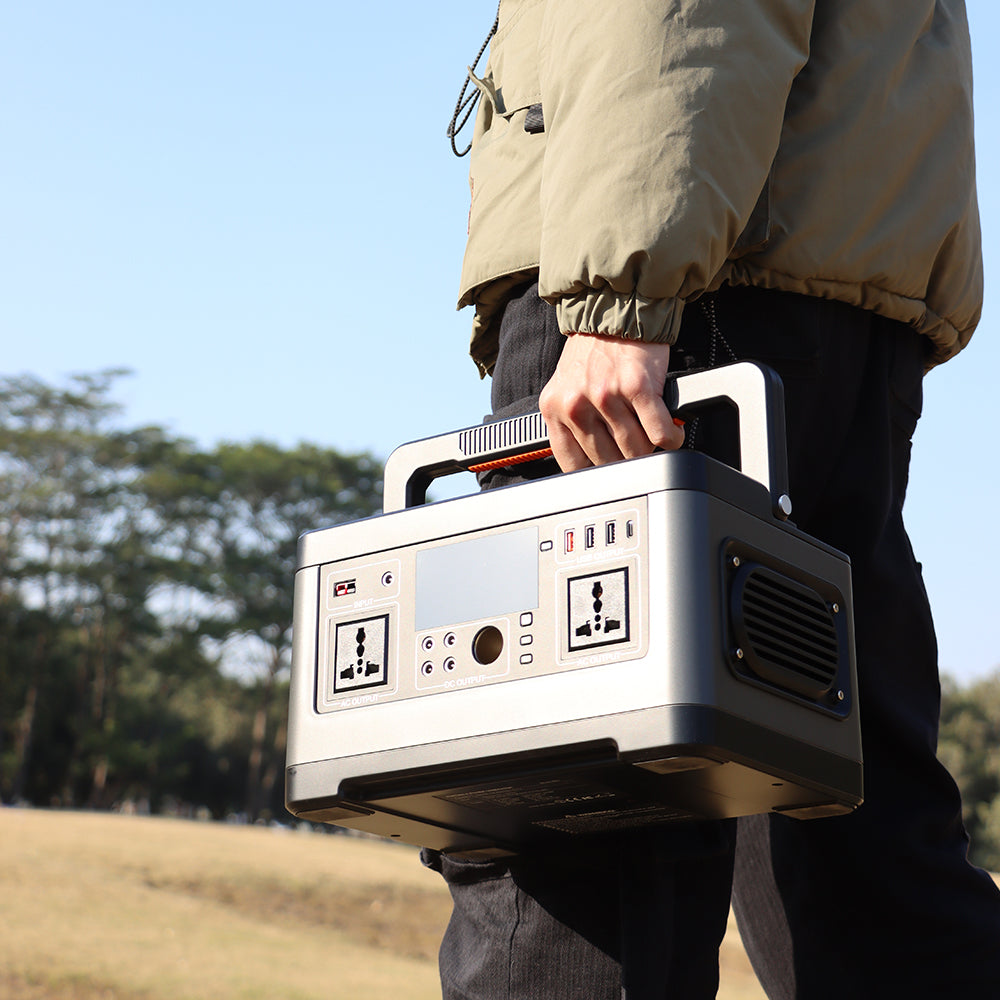 A person carries a portable power station by its handle across a grassy field.