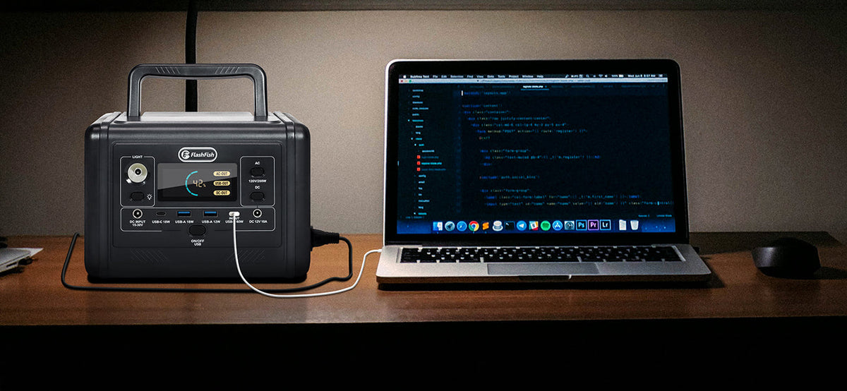 A portable power station and laptop sit side by side on a wooden desk.
